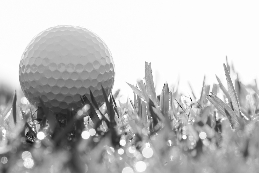 black and white photo of golf ball on grass with bokeh